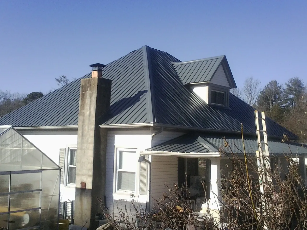 Dark blue standing seam metal roof on a white farmhouse with dormer — Slate & Tile Roof Repair by Roofing Brothers in Roland
