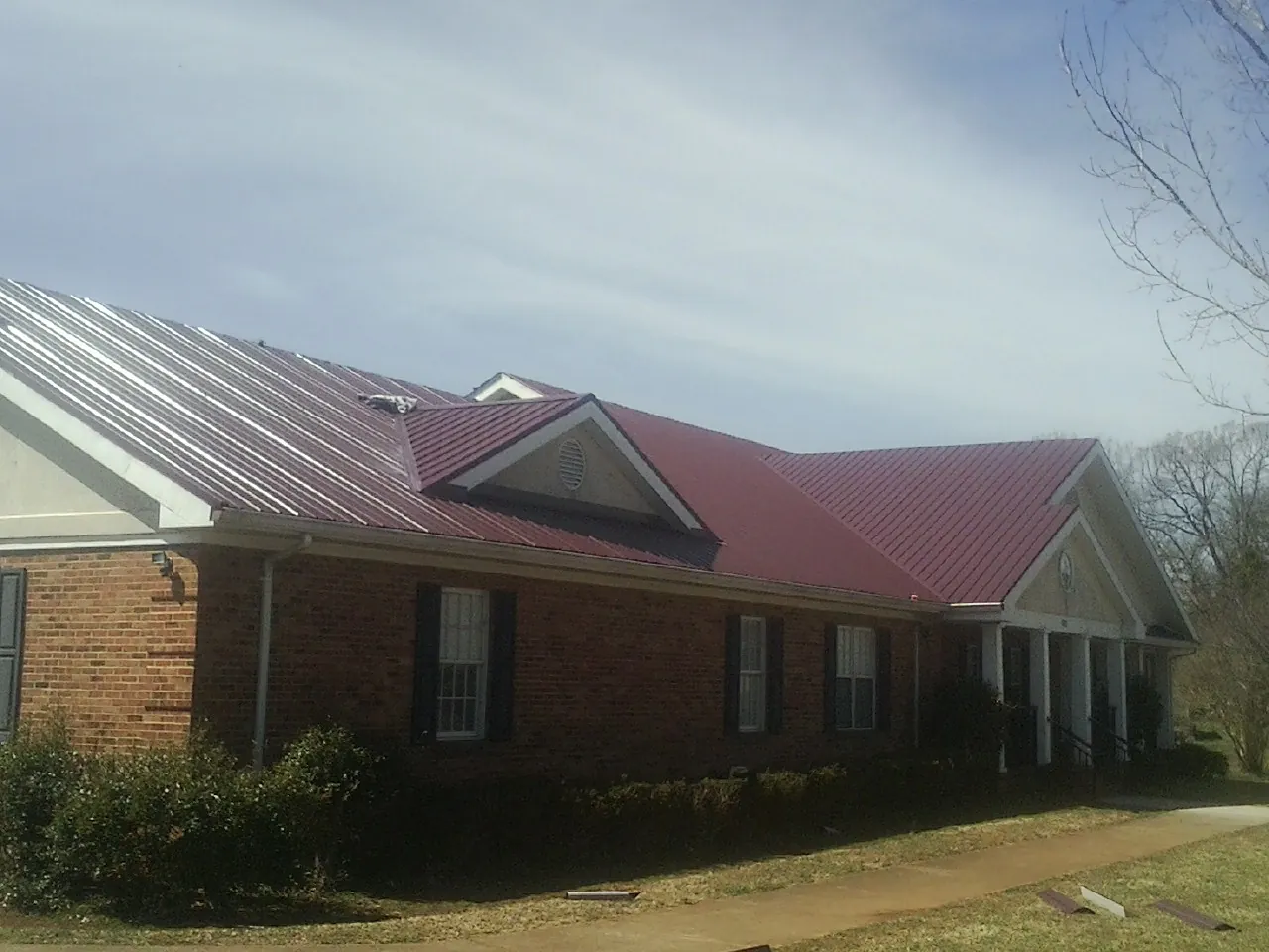 Red metal roof with gabled entries on a long brick building, from a Hail Damage Roof Repair job in Roland