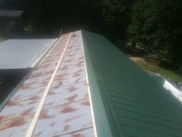 Old rusted panels beside newly installed green metal roofing — Wind Damage Roof Repair by Roofing Brothers in Roland