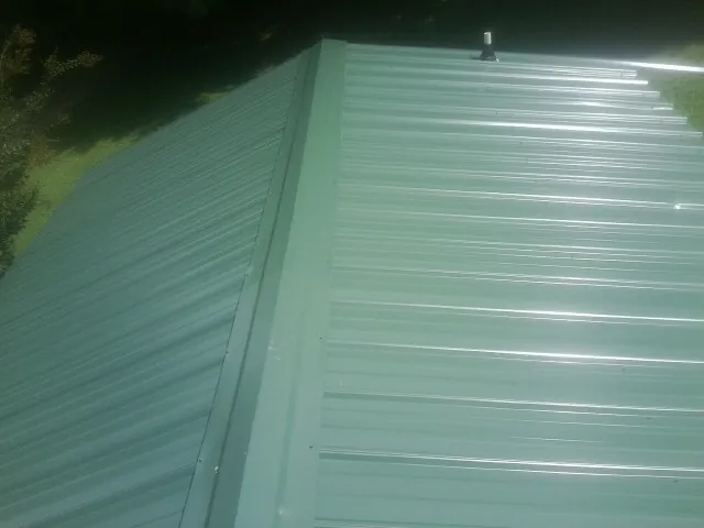 New green metal panels meeting at the ridge of a roof — Flat Roof Repair work by our crew in Roland