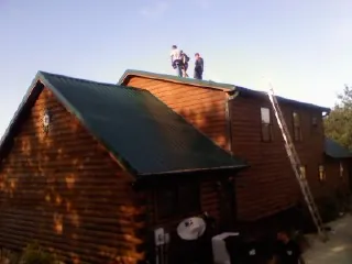 Crew on the ridge of a green metal roof on a two story log home in Roland