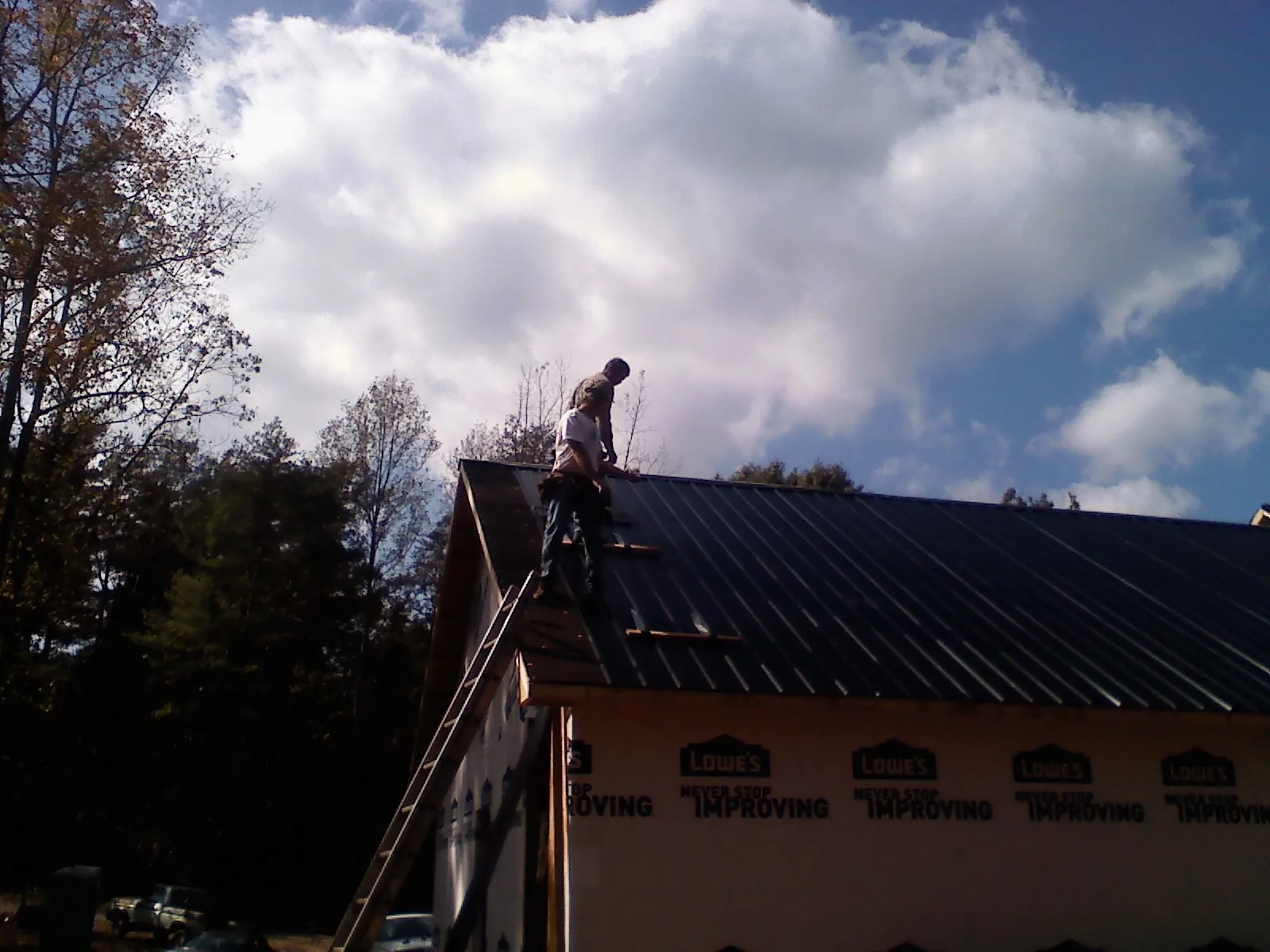 Roofer fastening dark metal panels high against a cloudy sky, from a Roof Inspection job in Roland