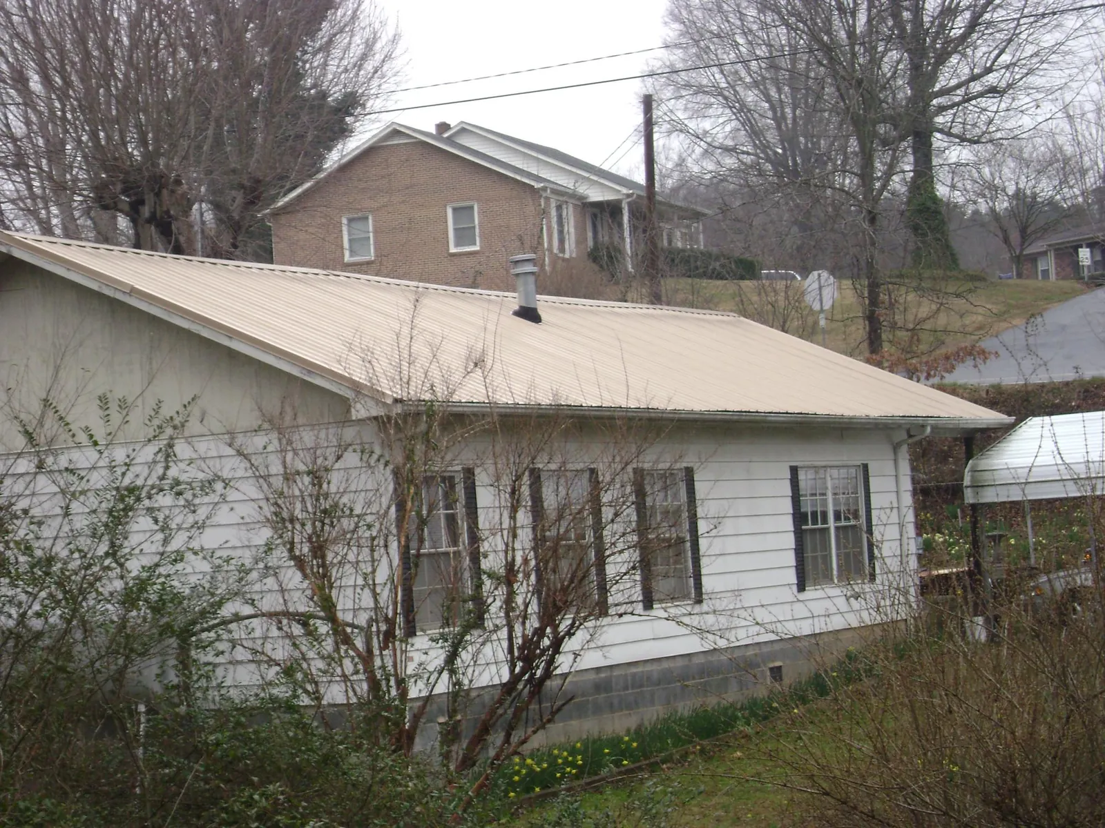 Tan metal roof on a white sided house set into a hillside — Commercial Roofing by Roofing Brothers in Roland