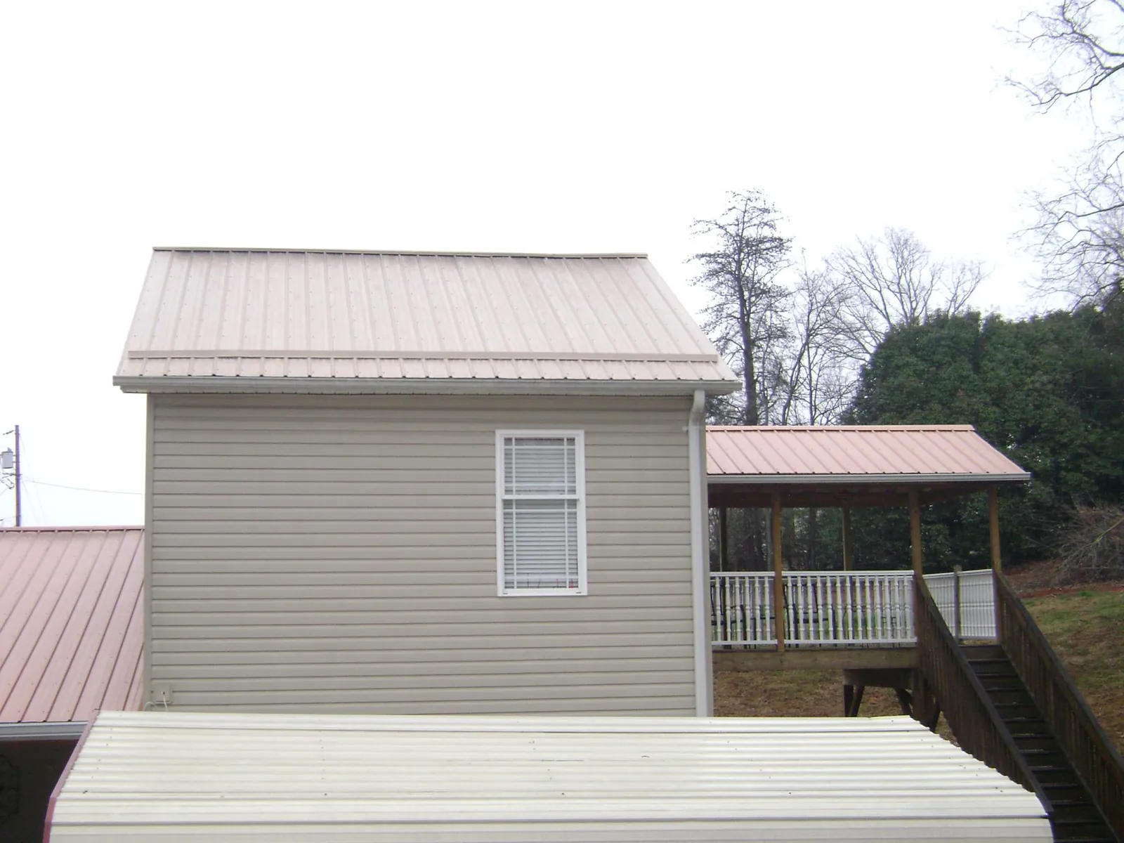 Tan metal roofs on a two story addition and attached porch, from a Roof Replacement job in Roland